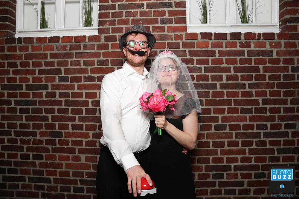 Eine Frau mit Schleifer und Blumenstrauss und ein Mann mit künstlicher Brille, Nase und Schnurrbart.